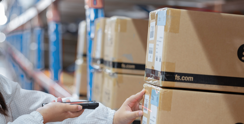 The image shows  customer order fulfilment warehouse distribution to supply chain solution and a staff member is scanning the box with a tool to prepare the goods for delivery.